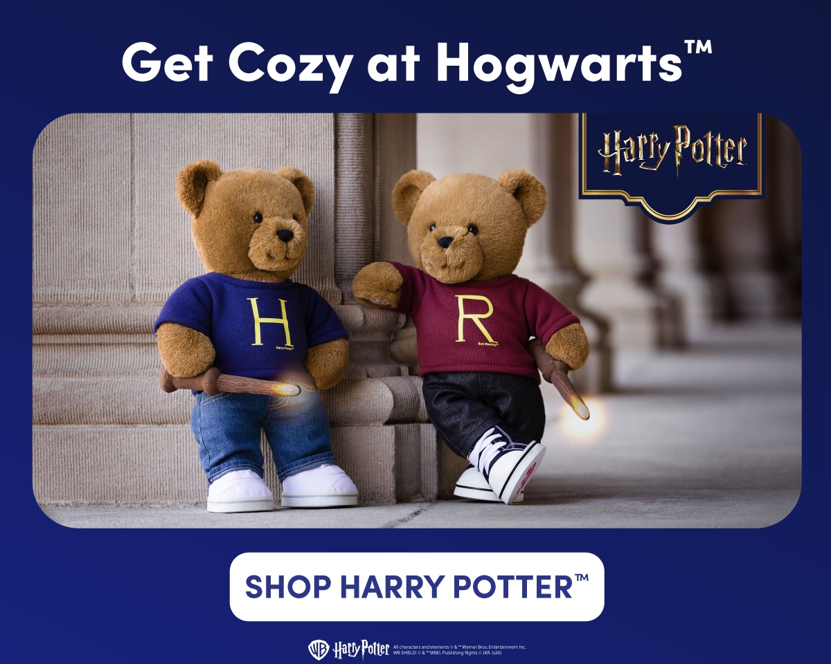 Harry Potter themed image with a navy blue background featuring two teddy bears posed in a Hogwarts-inspired setting with stone columns. One bear wears a blue sweater with a large gold H and jeans, while the other wears a burgundy sweater with a large gold R and dark pants. Both bears hold glowing wand accessories, with a Harry Potter logo and 25 Years of Magic emblem displayed beside them. Text reads: Get Cozy at Hogwarts™ Harry Potter 25 Years of Magic SHOP HARRY POTTER™