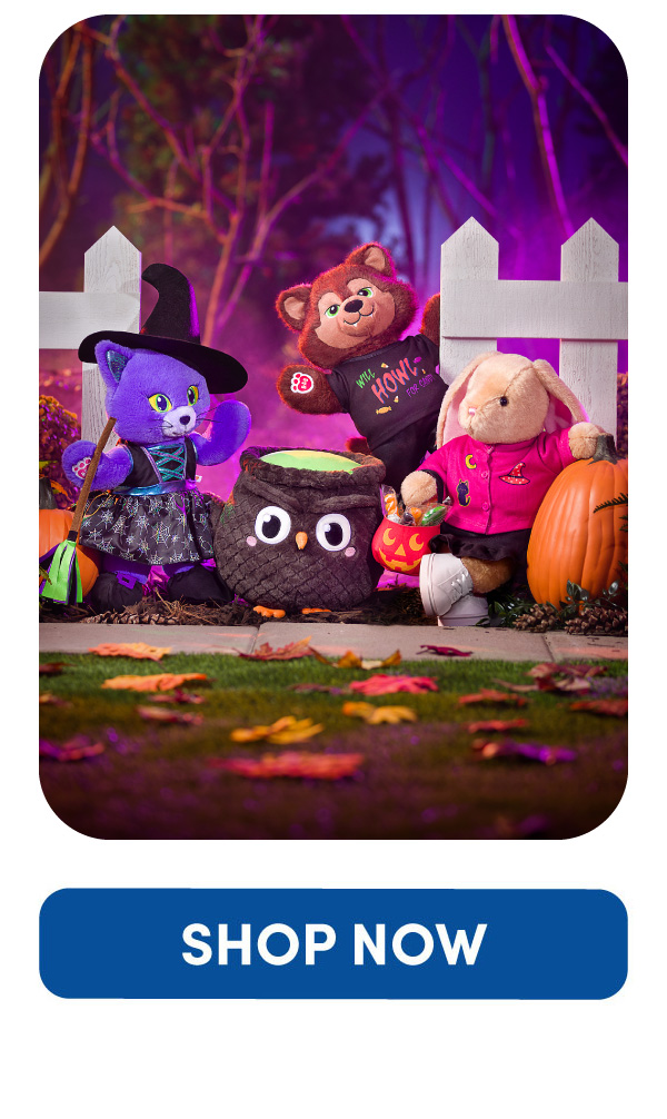 Four Halloween plush characters gathered around a Mashimals owl cauldron plush in a Halloween outdoor scene. A purple cat plush dressed as a witch, a brown bear plush wearing a Will HOWL for Candy T-shirt, a tan bunny plush holding a jack-o'-lantern candy bucket, and another plush carrying a green trick-or-treat bucket are posed beside pumpkins and a white fence against a purple and pink illuminated background.